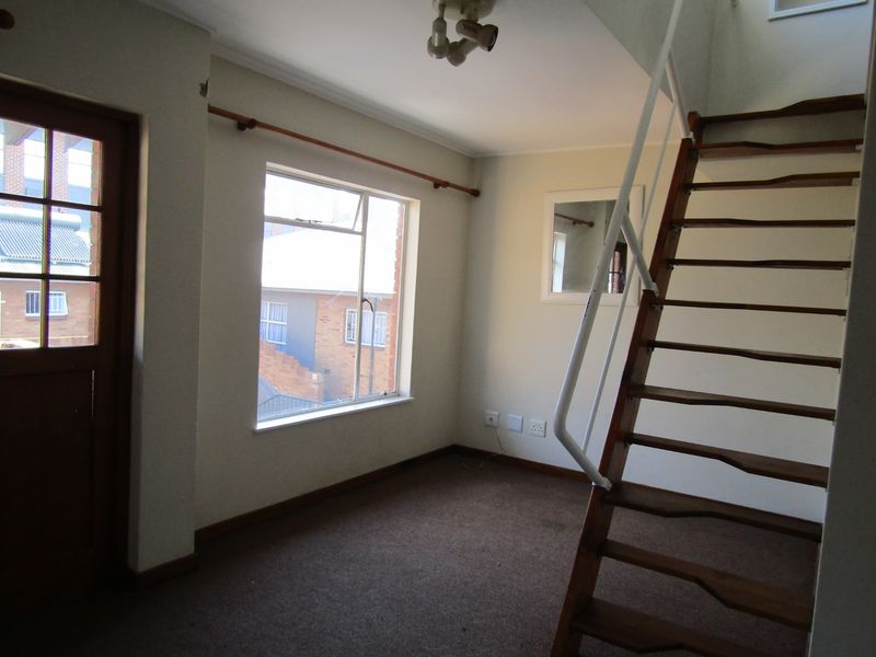 An empty living area featuring a timber staircase, carpeted flooring, and direct access to an exterior door.