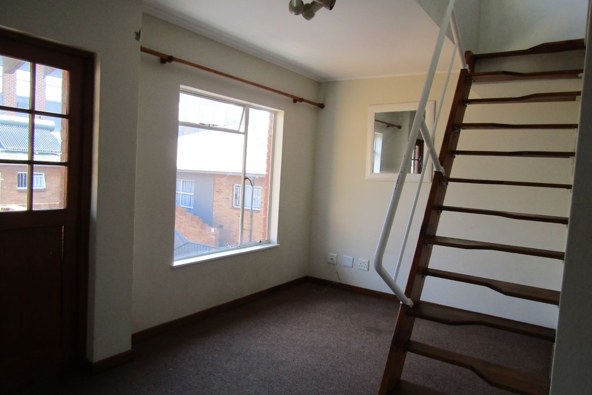 An empty living area featuring a timber staircase, carpeted flooring, and direct access to an exterior door.