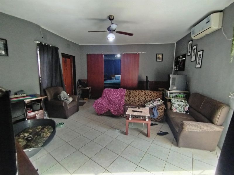 A living room featuring tiled flooring, a ceiling fan, and a wall-mounted air conditioning unit, providing a functional space for relaxation.