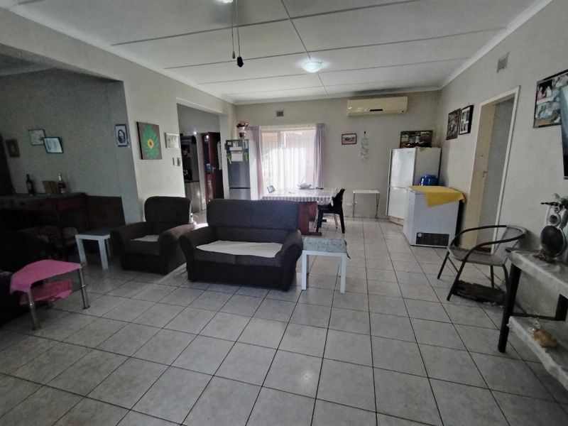 Spacious open-plan living area featuring tiled flooring, ceiling tiles, and a wall-mounted air conditioning unit.