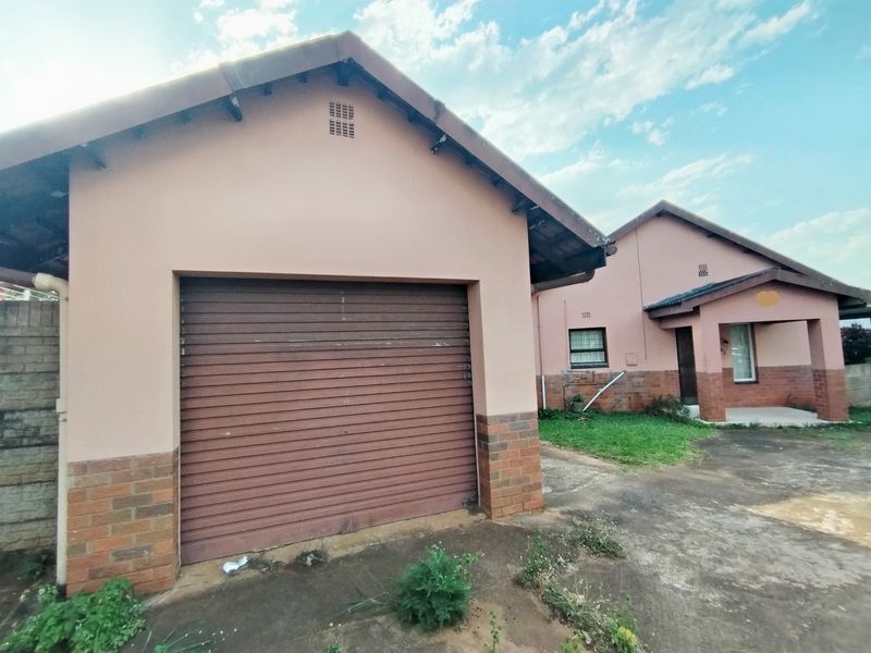 Front exterior view of a single-story house featuring a roller shutter garage door, brick base detailing, and a concrete driveway.