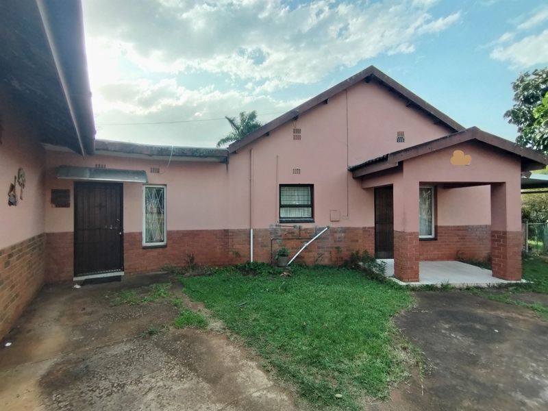 Rear view of a single-story house featuring a brick and plaster facade, covered porch area, and concrete driveway with surrounding lawn.