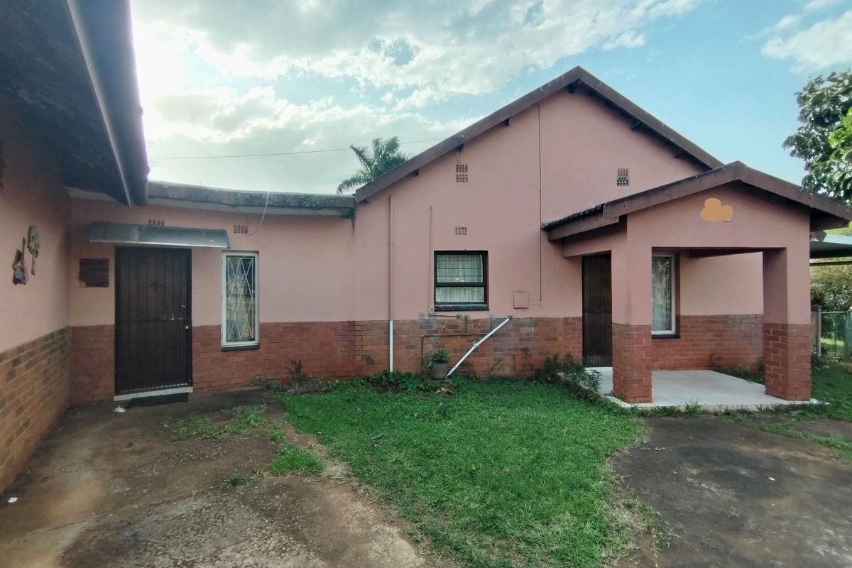 Rear view of a single-story house featuring a brick and plaster facade, covered porch area, and concrete driveway with surrounding lawn.