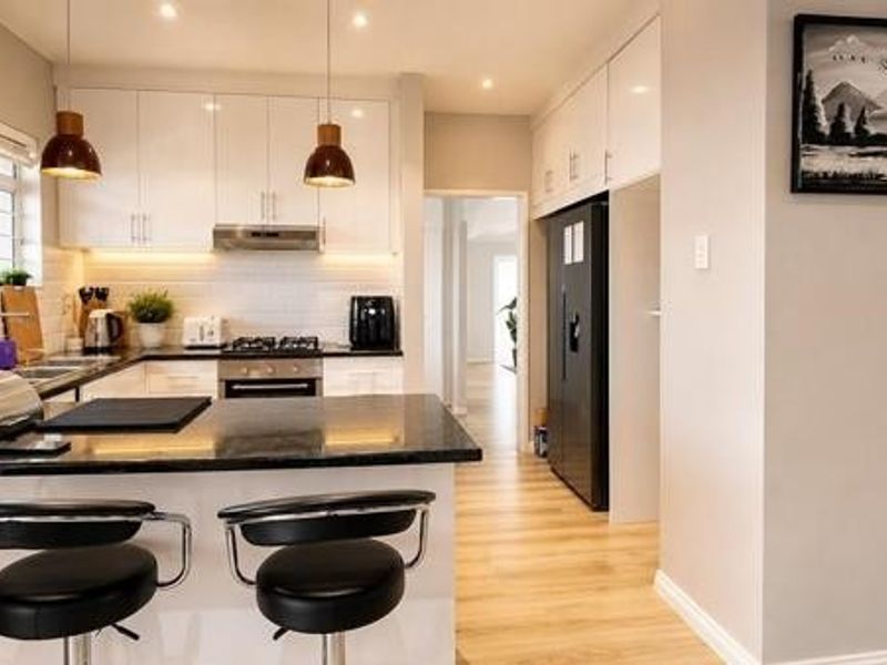 Modern kitchen featuring white cabinetry, granite countertops, stainless steel appliances, and a breakfast bar, seamlessly integrated with the living area.