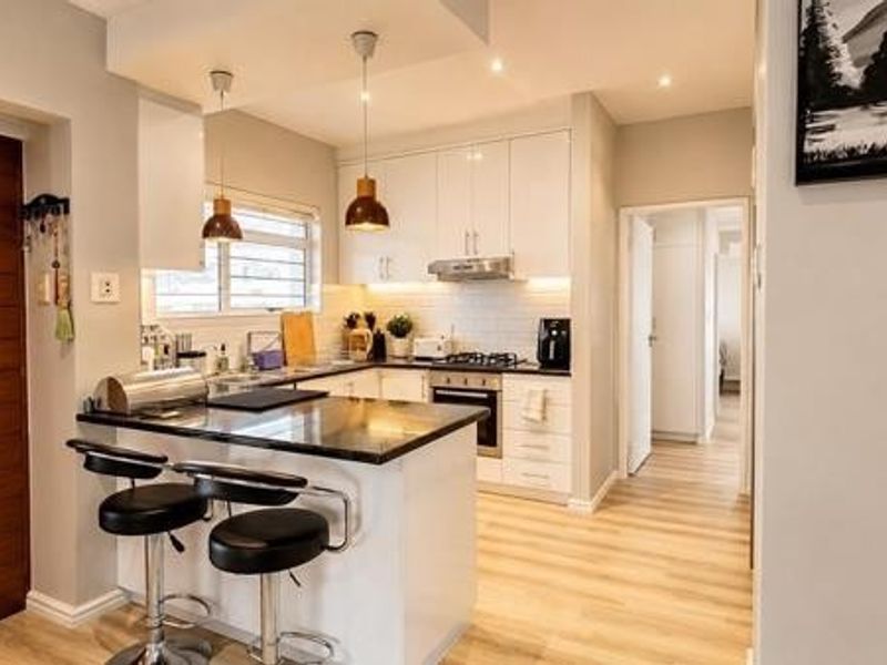 Modern kitchen featuring sleek white cabinetry, stone countertops, integrated appliances, and a functional breakfast bar, finished with contemporary lighting and light wood-look flooring.