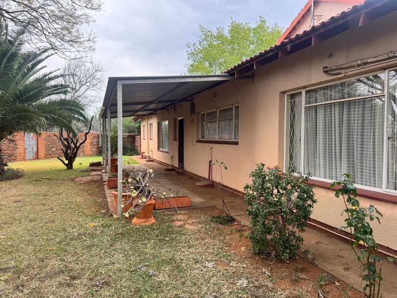 Rear view of the house featuring a covered patio area, tiled roof, and a spacious garden with a brick boundary wall.