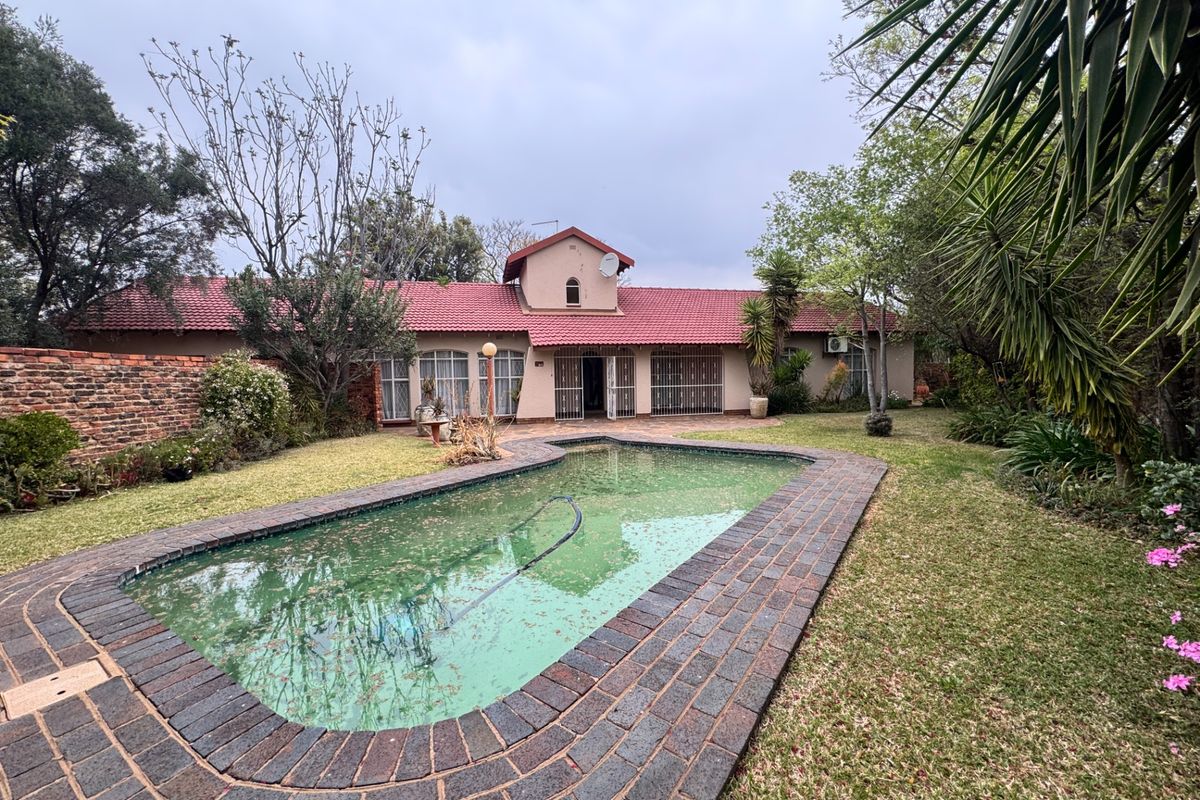 Rear view of the property featuring a swimming pool with brick coping, a large garden, and a tiled roof house exterior.