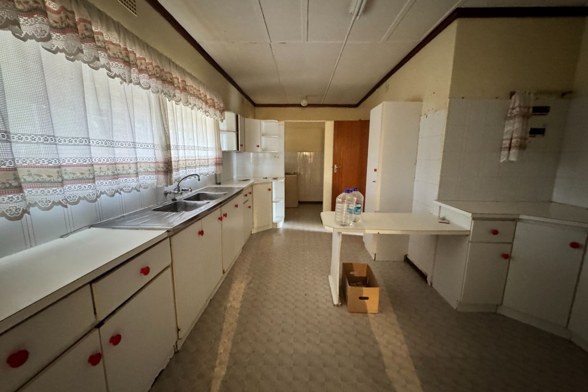 A dated, empty kitchen featuring original cabinetry, double basin sink, and tiled splashbacks, offering significant potential for a modern renovation.