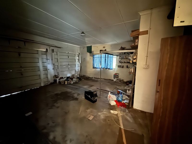 A spacious, unfinished garage area featuring a sectional door, concrete flooring, and built-in storage shelving, offering potential for workshop or vehicle storage use.