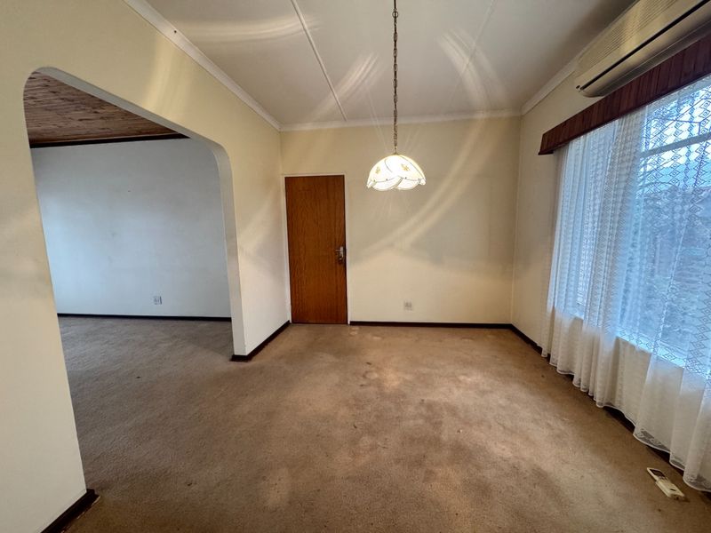 An empty living room featuring carpet flooring, an archway leading to an adjacent space, and a wall-mounted air conditioning unit.