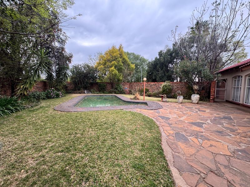 A private backyard featuring a swimming pool, stone-paved patio area, and established garden enclosed by a brick boundary wall.