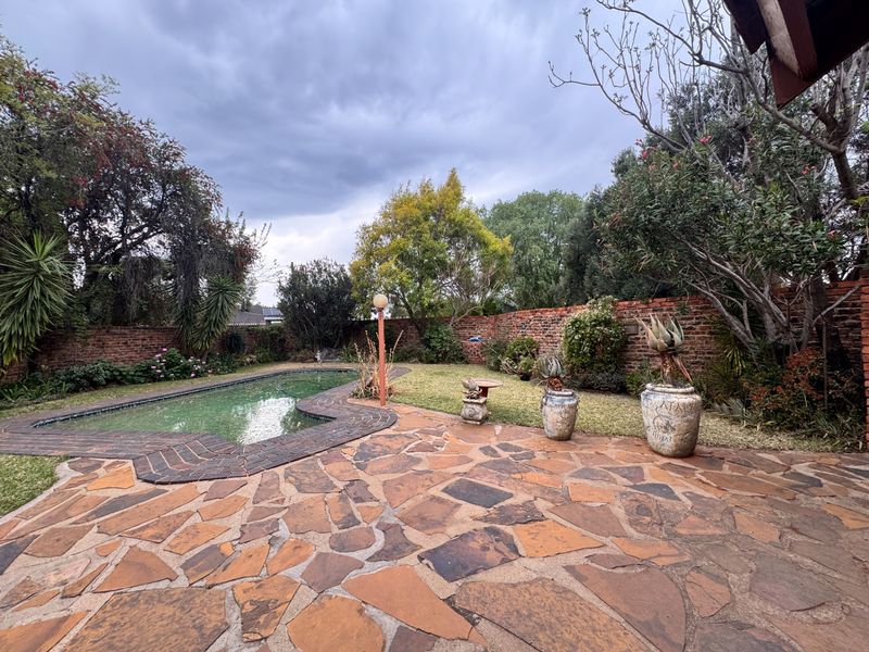 A private outdoor pool area featuring a swimming pool, flagstone patio, and established garden enclosed by a brick boundary wall.