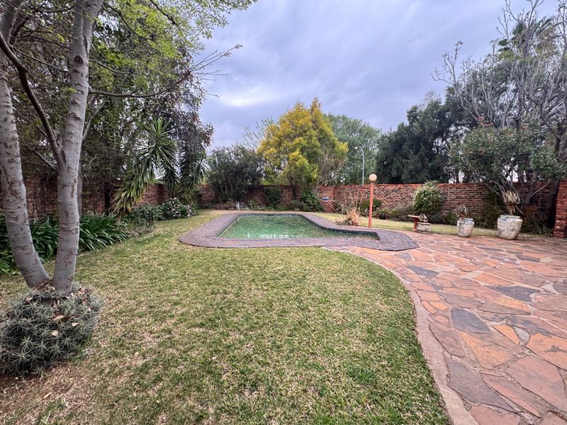 A private backyard featuring a swimming pool, stone paved patio area, and established garden surrounded by a brick boundary wall.
