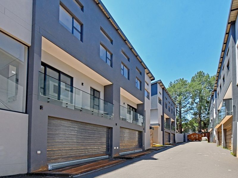 Modern multi-level residential complex featuring contemporary grey facades, glass balcony balustrades, and secure roller shutter garage doors.
