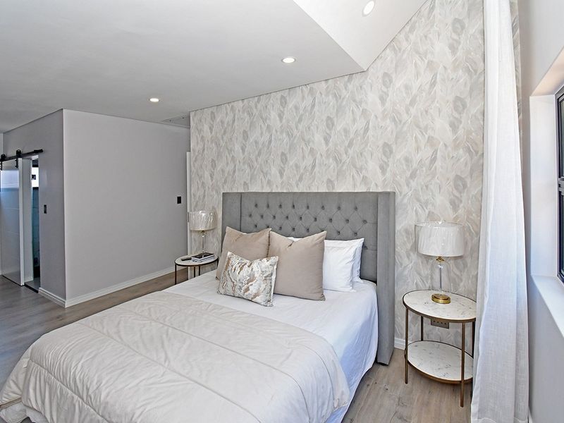 A modern, well-maintained bedroom featuring laminate flooring, recessed downlighting, and a stylish feature wallpaper wall.