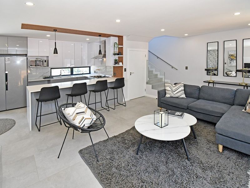 Modern open-plan living area featuring a sleek kitchen with island seating, tiled floors, and a contemporary staircase with glass balustrade.