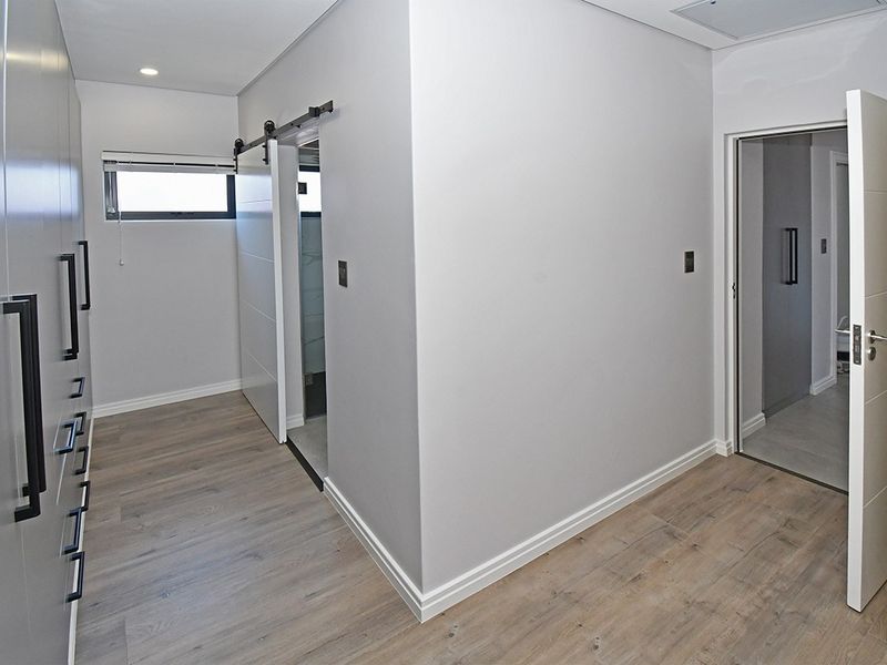 A modern, empty bedroom featuring light wood-look laminate flooring, extensive built-in cabinetry, and a sleek sliding barn door leading to an en-suite bathroom.
