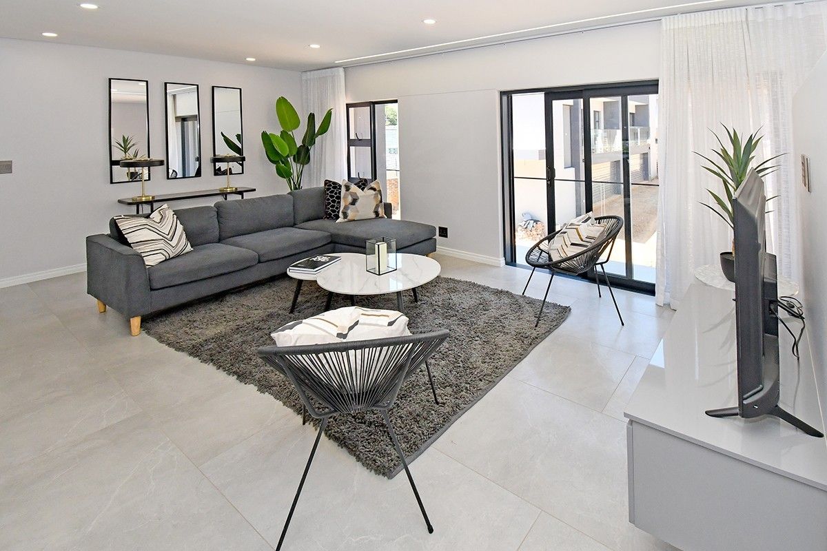 A bright and modern living room featuring large format floor tiles, recessed downlighting, and sliding glass doors providing access to the exterior.