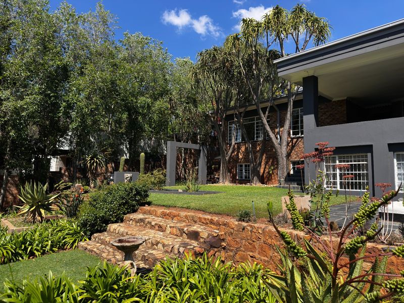 A well-maintained rear garden featuring a stone retaining wall, tiered lawn, and a covered patio area attached to the brick-clad residence.