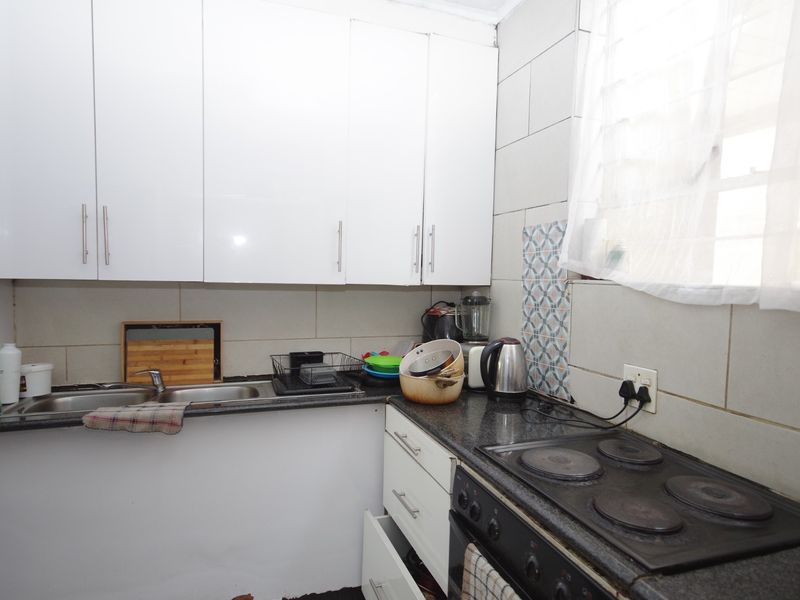Compact kitchen featuring white cabinetry, granite countertops, a stainless steel sink, and an integrated electric hob with tiled backsplash.