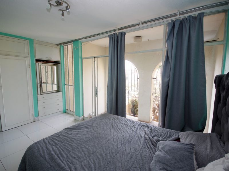 Bedroom featuring built-in cupboards, tiled flooring, and arched windows with security bars, offering a functional space with potential for cosmetic updates.
