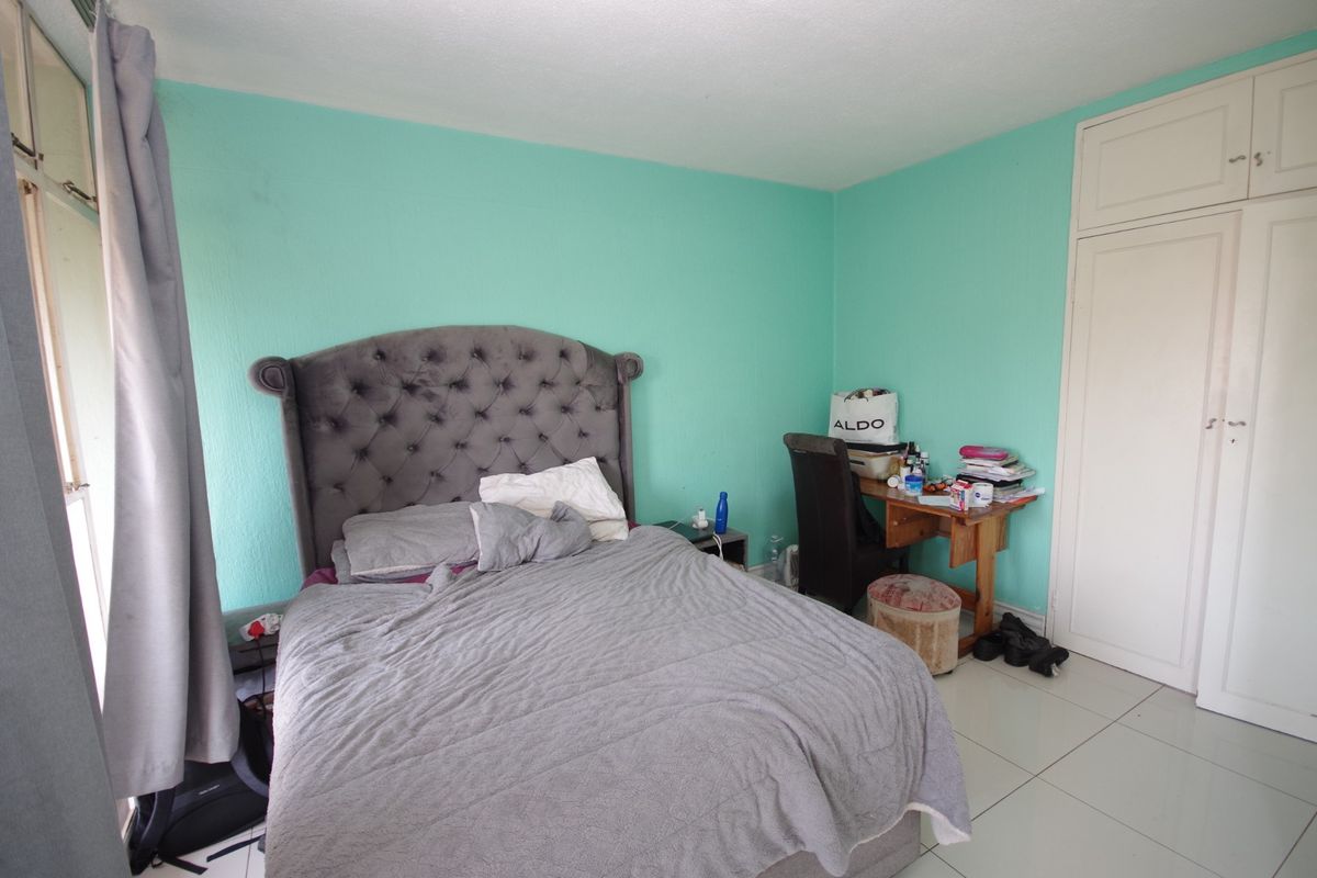 A bedroom featuring tiled flooring and a built-in wardrobe, currently finished with bright teal wall paint.