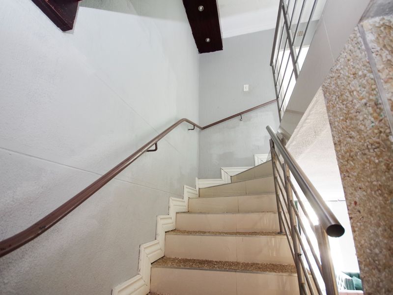 A staircase featuring tiled steps, a metal handrail, and decorative ceiling molding, providing access between levels in the apartment.
