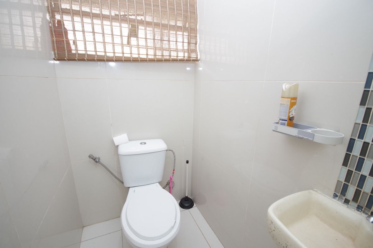A compact bathroom featuring tiled walls and flooring, equipped with a standard toilet and a wall-mounted basin.