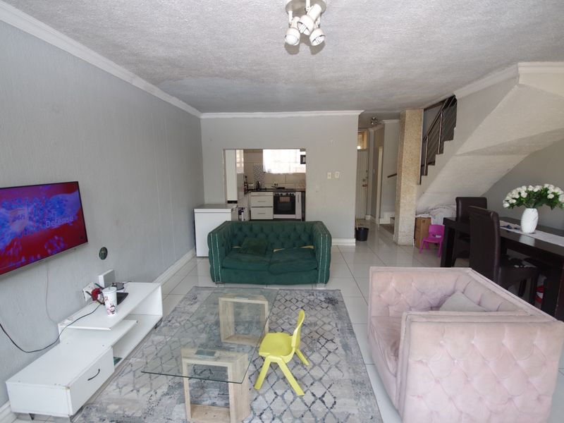 Open-plan living and dining area featuring tiled floors, a staircase with metal railing, and a view through to the kitchen.