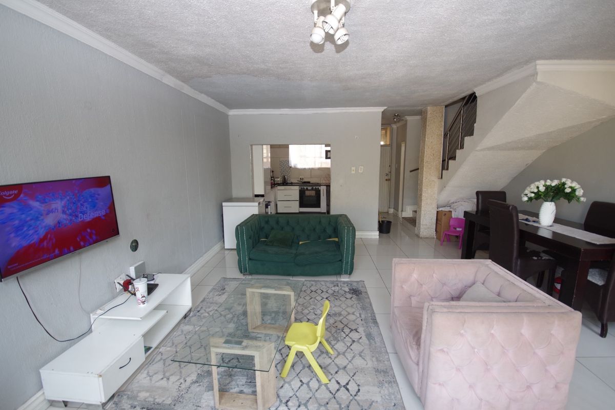 Open-plan living and dining area featuring tiled floors, a staircase with metal railing, and a view through to the kitchen.