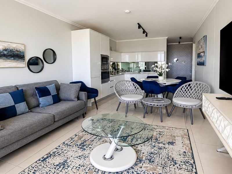 Modern open-plan living and dining area featuring high-gloss kitchen cabinetry, integrated appliances, mirrored splashbacks, and sleek tiled flooring throughout.