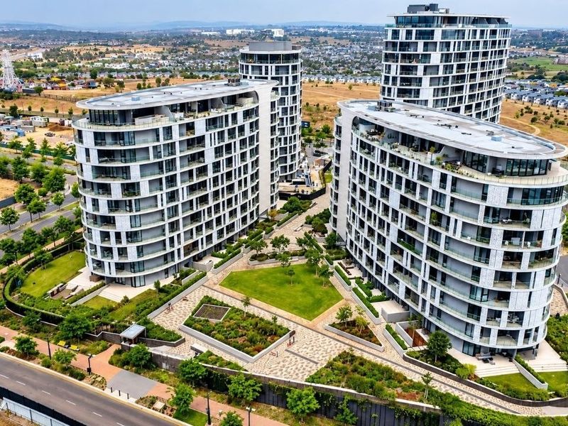 Aerial view of a modern apartment complex featuring multiple high-rise buildings, landscaped communal gardens, and paved outdoor areas in a suburban setting.