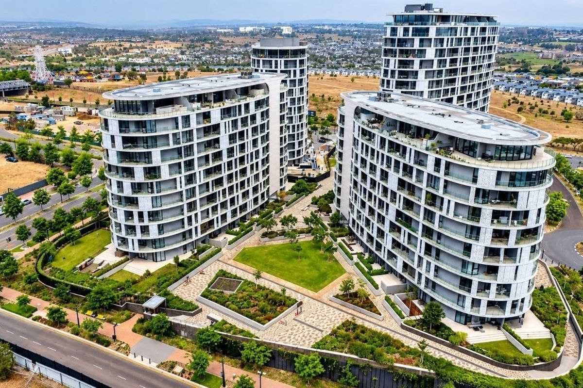 Aerial view of a modern apartment complex featuring multiple high-rise buildings, landscaped communal gardens, and paved outdoor areas in a suburban setting.