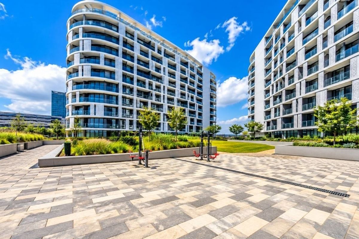 A well-maintained communal courtyard featuring paved walkways, landscaped garden beds, and outdoor fitness equipment between modern apartment buildings.