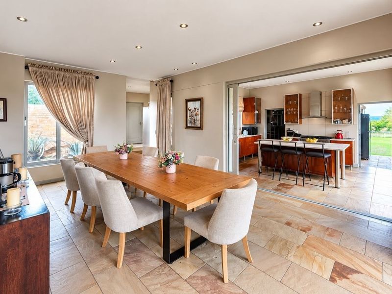 Spacious open-plan dining area featuring natural stone flooring, a stone feature wall, and seamless flow into a well-appointed kitchen with modern cabinetry.