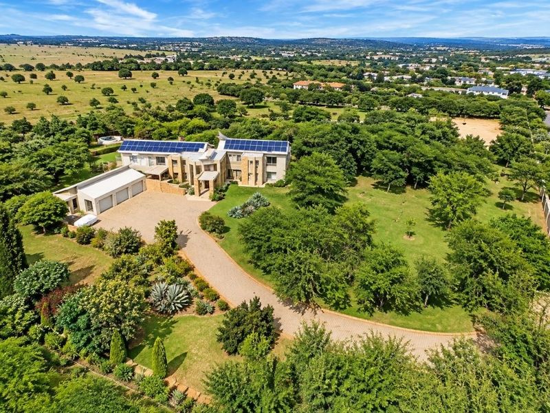 Aerial view of a large residential property featuring extensive landscaped grounds, a long paved driveway, triple garage, and roof-mounted solar panels.