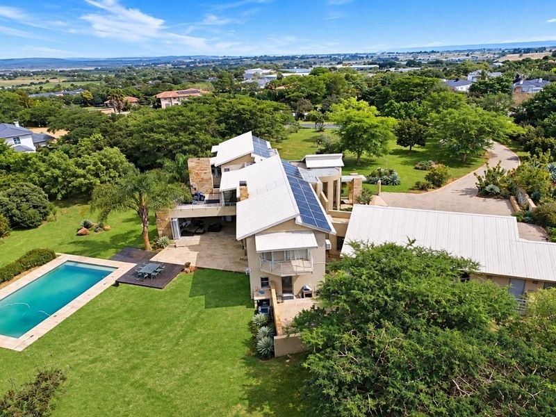 Aerial view of a large residential property featuring a swimming pool, extensive landscaped gardens, solar panels, and a spacious paved driveway.