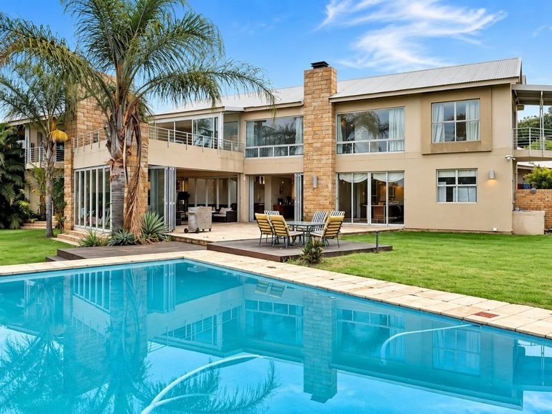 Spacious rear exterior featuring a large swimming pool, expansive lawn, stone-clad pillars, and a covered patio with bi-fold doors leading into the home.