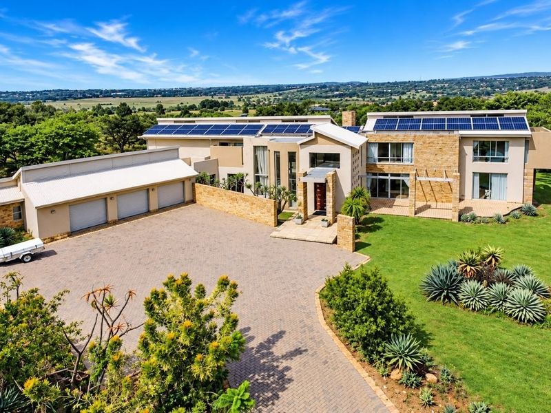 Aerial view of a modern luxury residence featuring extensive solar panel arrays, a triple garage, paved driveway, and landscaped grounds.