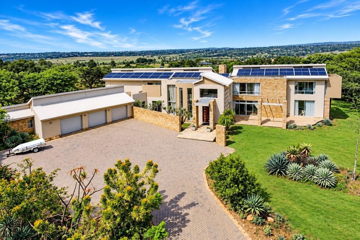 Aerial view of a modern luxury residence featuring extensive solar panel arrays, a triple garage, paved driveway, and landscaped grounds.