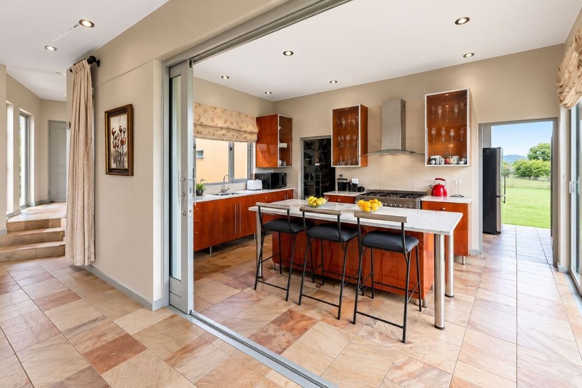 Modern kitchen featuring wood cabinetry, stone countertops, a central island with breakfast bar seating, and seamless access to the outdoor patio area.