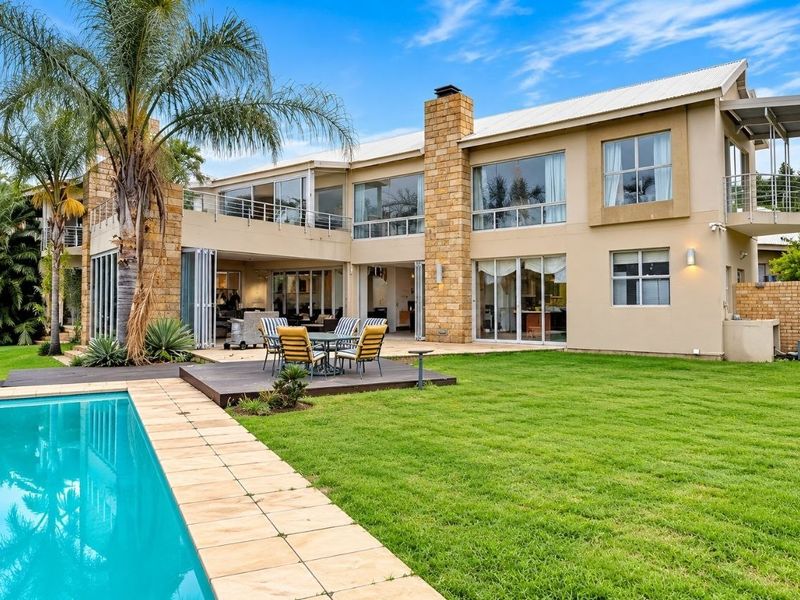 Spacious rear exterior featuring a swimming pool, timber deck, stone-clad chimney, and large sliding doors leading to the main living areas.