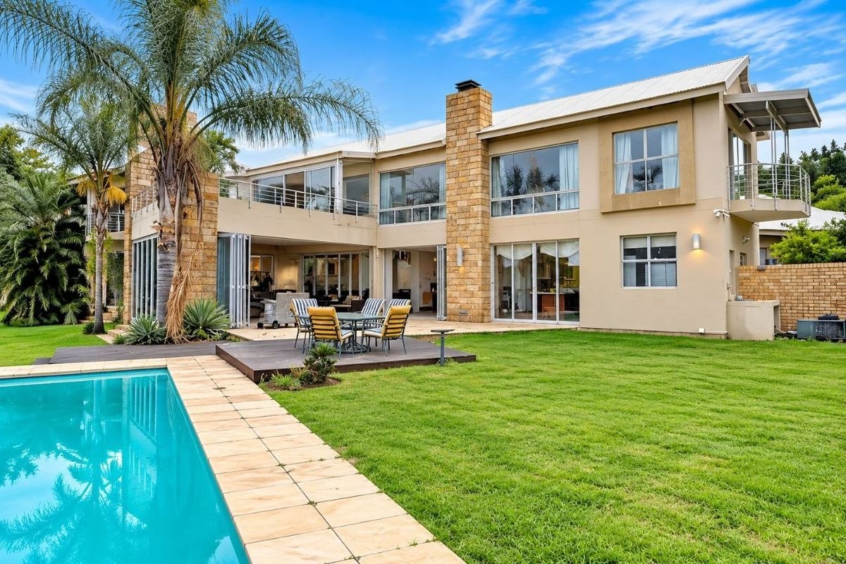 Spacious rear exterior featuring a swimming pool, timber deck, stone-clad chimney, and large sliding doors leading to the main living areas.