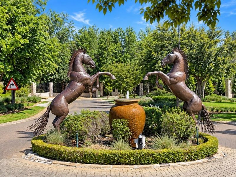 A well-maintained entrance to the property featuring a paved driveway, landscaped garden, and a decorative water feature with horse sculptures.