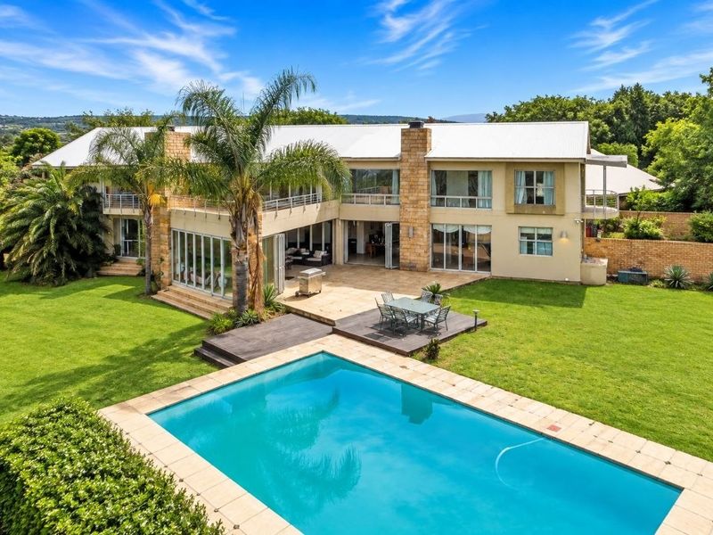 Spacious rear exterior view featuring a large swimming pool, expansive lawn, timber decking, tiled patio, and a multi-level residence with stone accents.
