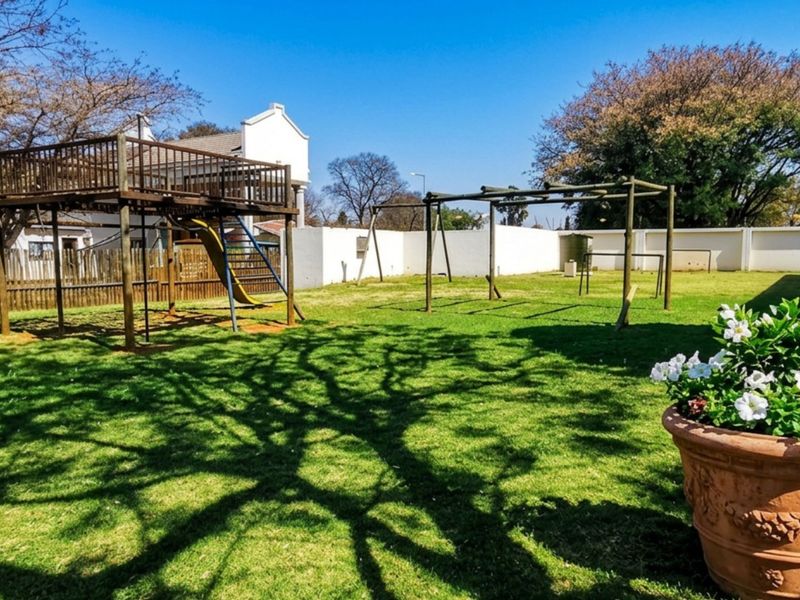 A spacious private garden featuring a large lawn area and a wooden jungle gym structure, enclosed by perimeter walls and fencing.
