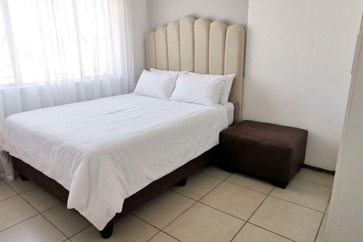 A clean and well-maintained bedroom featuring neutral tiled flooring and large windows with sheer curtains, providing a bright and comfortable living space.