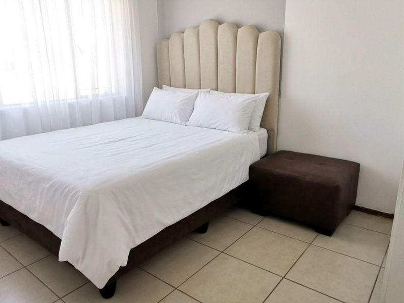 A clean and well-maintained bedroom featuring neutral tiled flooring and large windows with sheer curtains, providing a bright and comfortable living space.