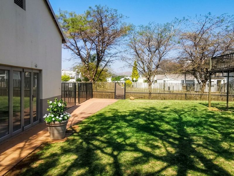 Rear garden area featuring a lawn, timber decking, and aluminium stacker doors leading into the home, complemented by a raised wooden play structure.