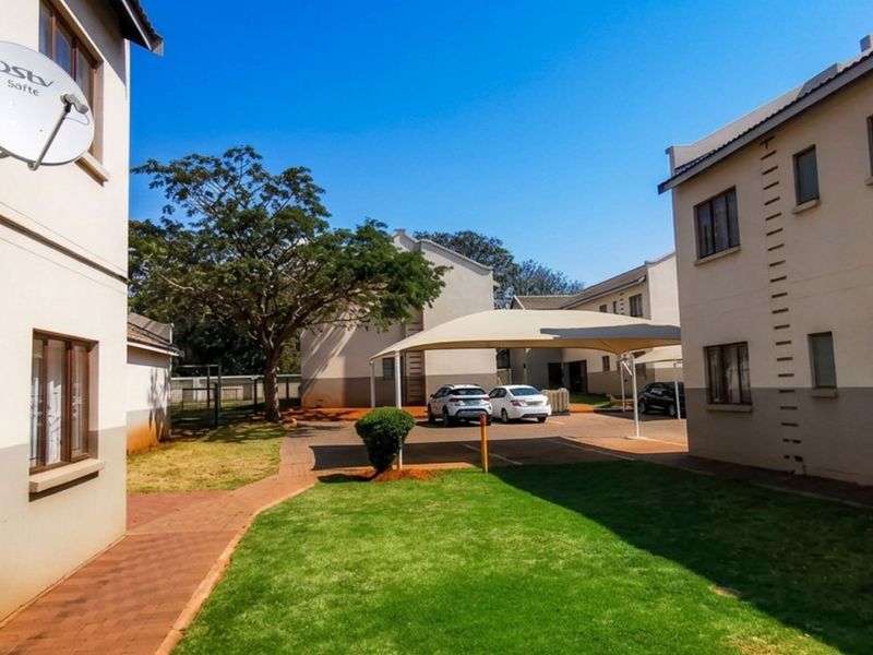 A view of the townhouse complex exterior featuring a shared lawn, paved walkways, and covered parking bays.